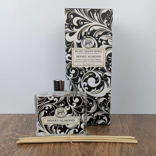 A reed diffuser set with a black and white floral patterned box, a clear glass bottle, and a bundle of reeds tied with a string.