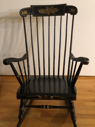 Black rocking chair with decorative elements on a wooden floor.
