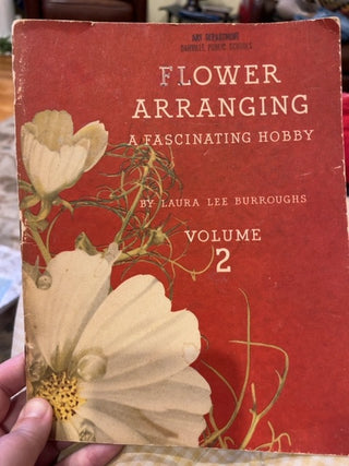 Book titled 'Flower Arranging: A Fascinating Hobby' by Laura Lee Burroughs Volume 2 with floral design on a red background.