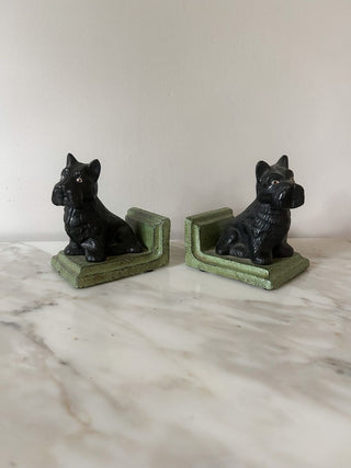 Two black dog figurines on green stands on a marble surface with a white background