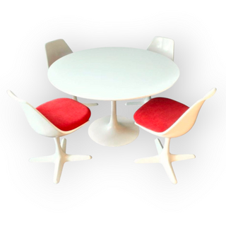Round white table with four chairs, three of which have red cushions on a white background
