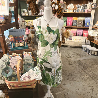 Magnolia Petals Apron with pockets featuring green foliage and magnolia blooms | JSQ Mercantile – a women’s boutique and gift shop in La Grange, IL.